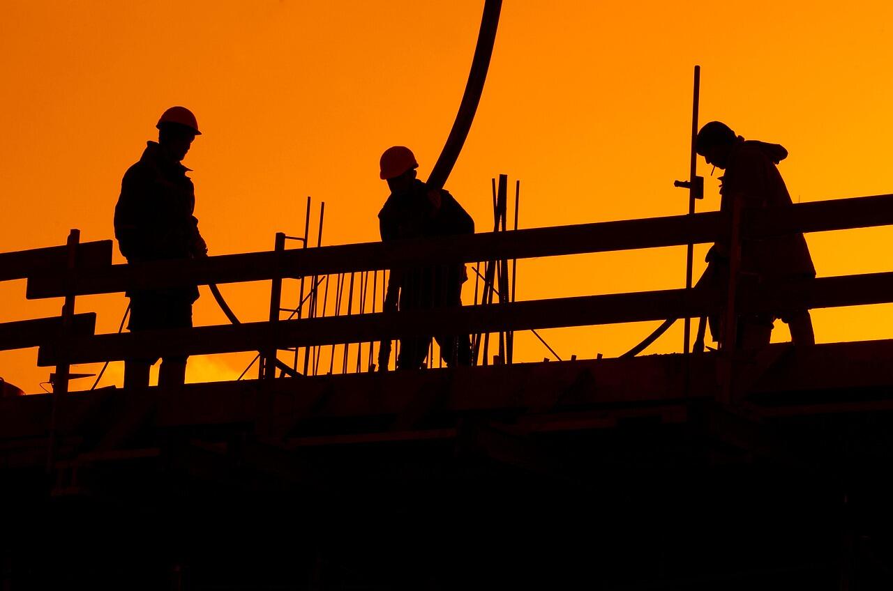 Construction workers silhouetted against an orange sky at the end of the day